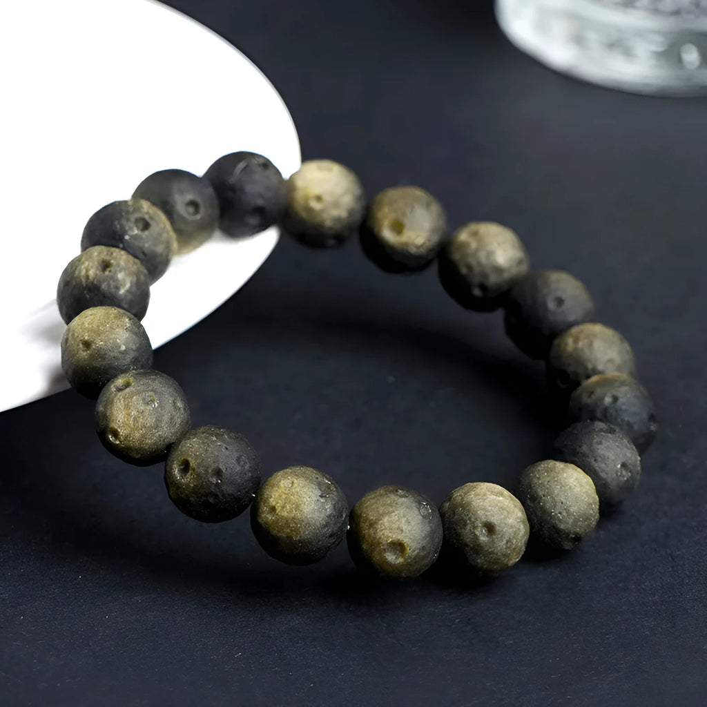 A natural obsidian crater ball bracelet in gold or silver meteorite colour on a wrist, showing textured bead detail.