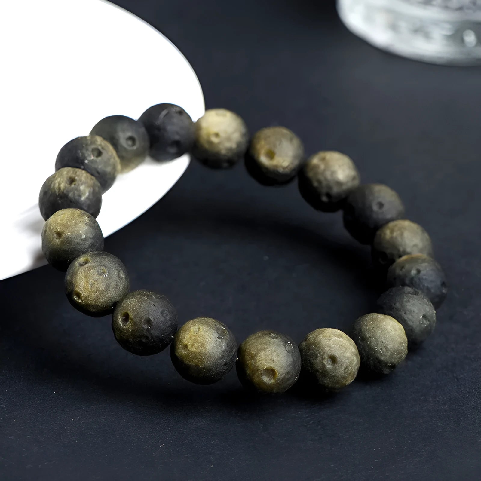 A natural obsidian crater ball bracelet in gold or silver meteorite colour on a wrist, showing textured bead detail.