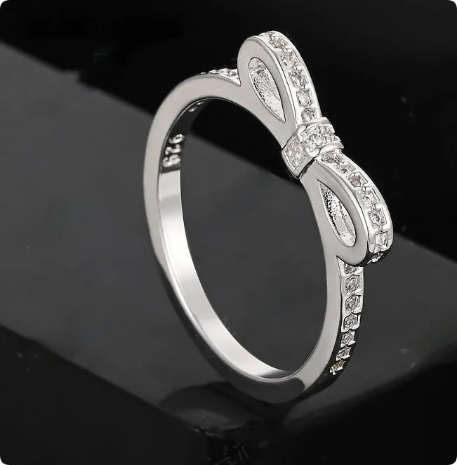 Close-up of a silver bow-shaped ring with sparkling clear zircon crystals on a person's finger.