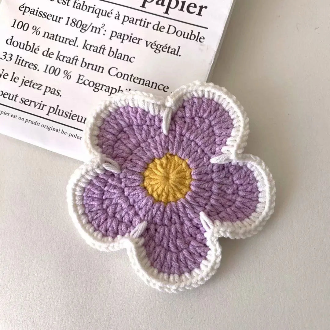 Set of five handmade woven flower placemats in blue, green, orange, pink, and purple colours on a wooden table.