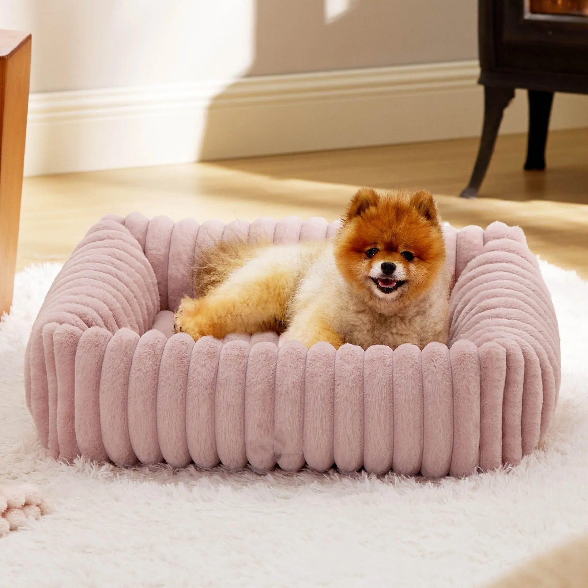 Beige plush pet bed with raised bolster sides for cats and dogs, shown in a home setting.