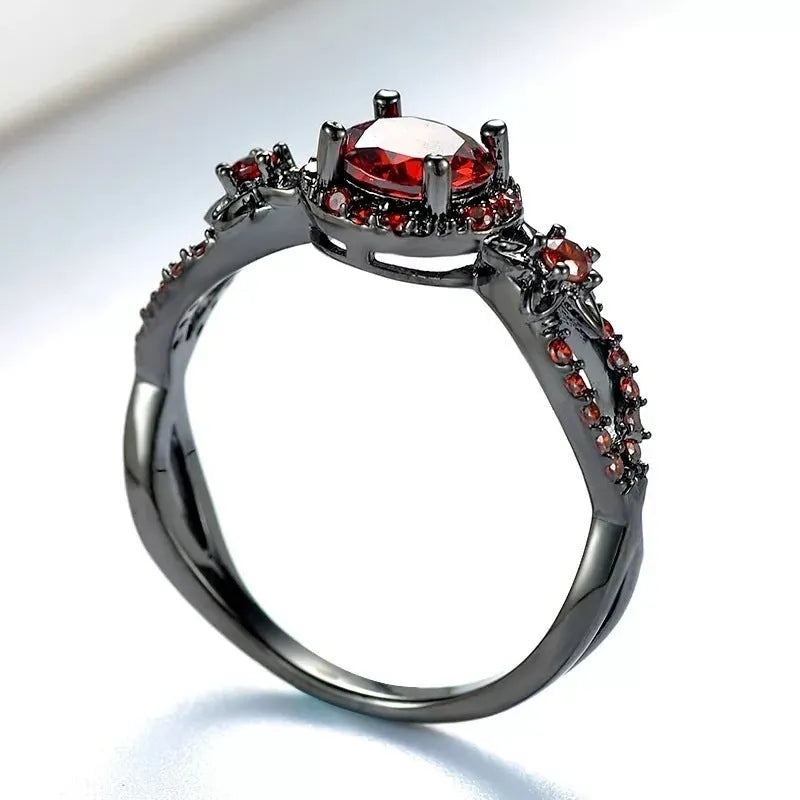 Black gold plated copper ring with round red zircon stone and wave-shaped band on finger