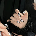 Black false nails with pink hand-painted peach hearts and bow design, shown in a cat's eye style.