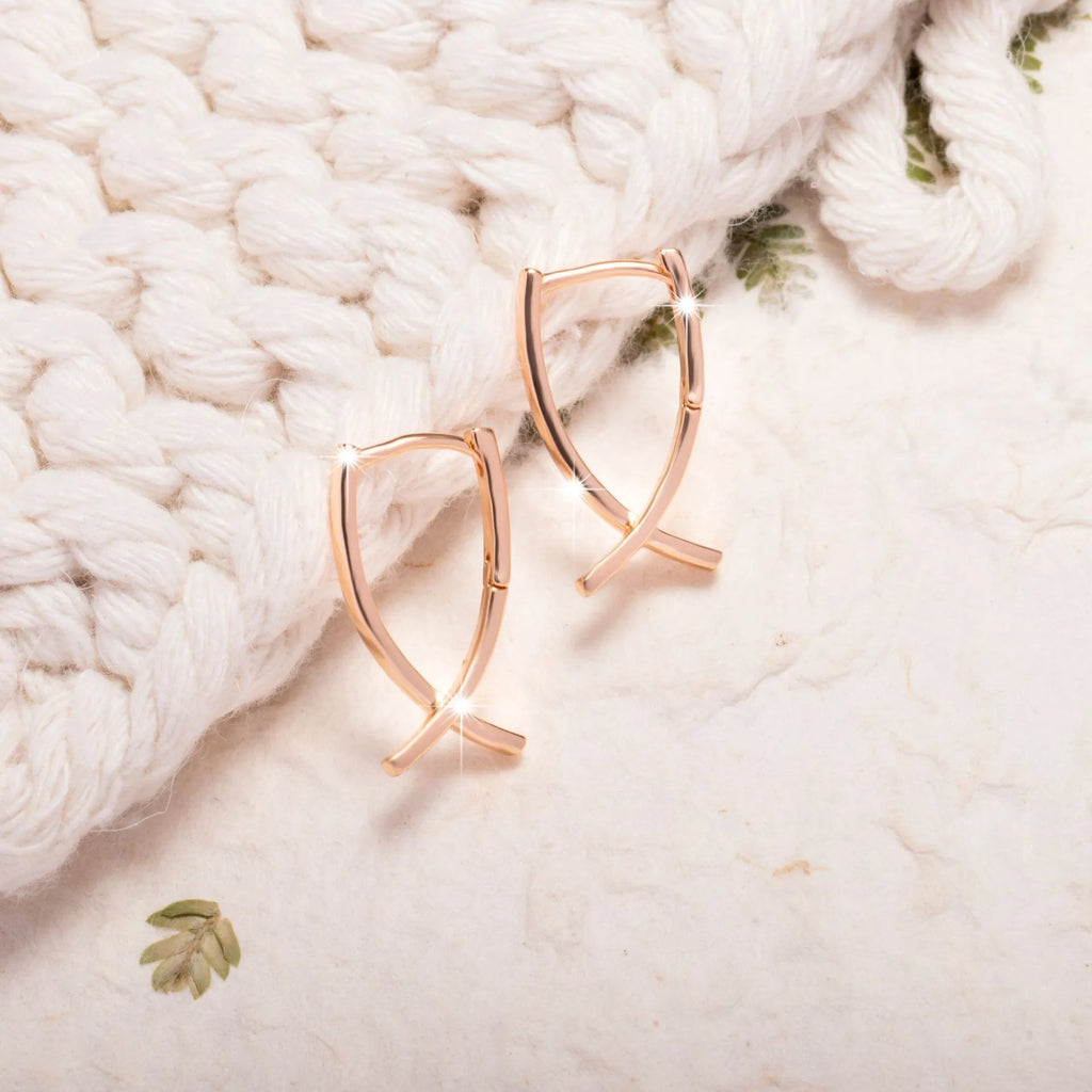 Rose gold cross shaped earrings on a plain background.