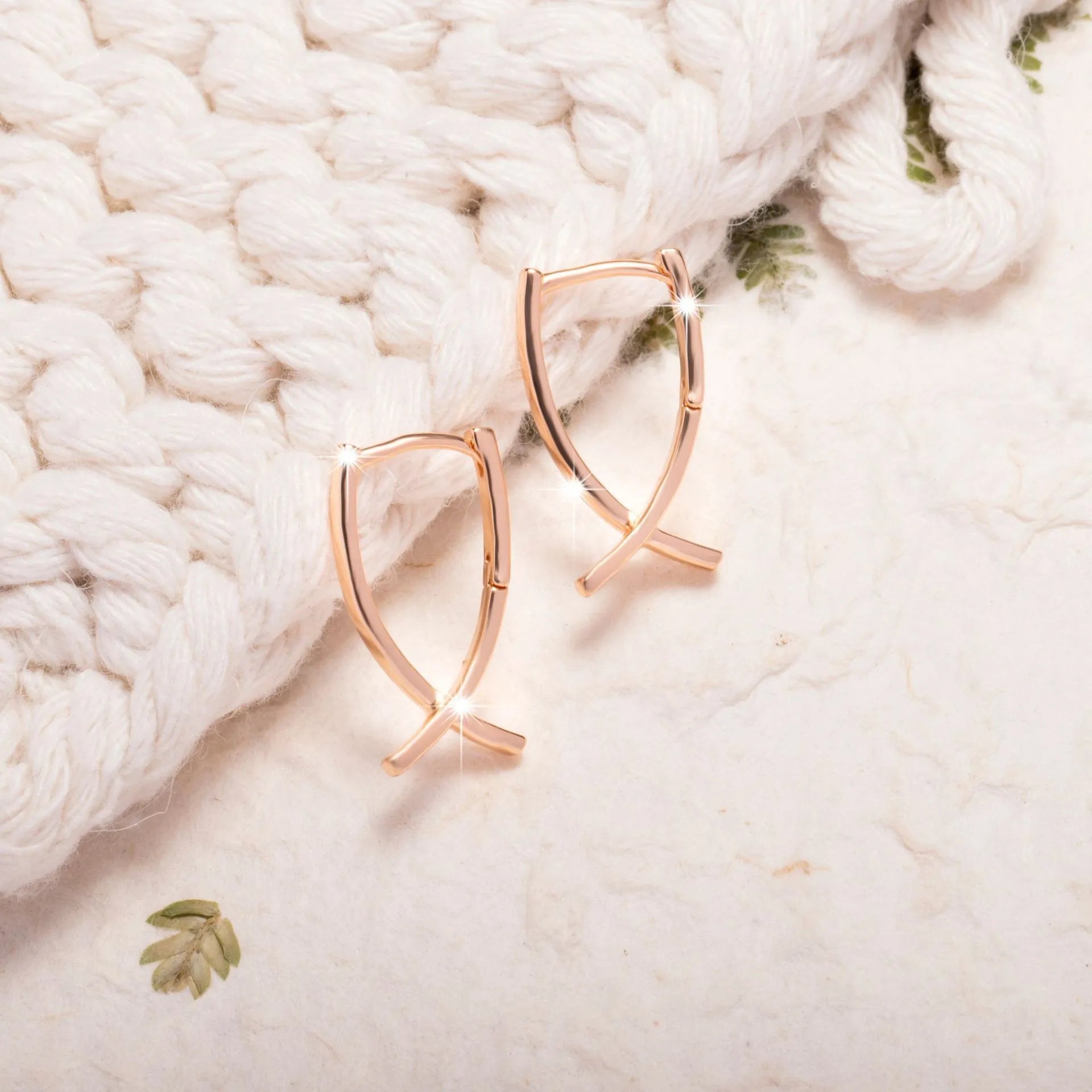 Rose gold cross shaped earrings on a plain background.