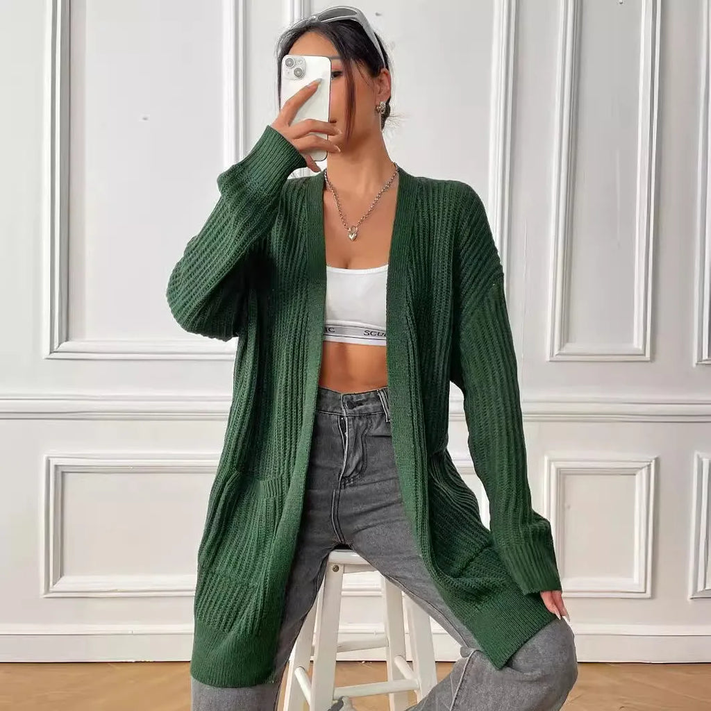 A woman wearing a dark green, mid-length acrylic cardigan with two front pockets.