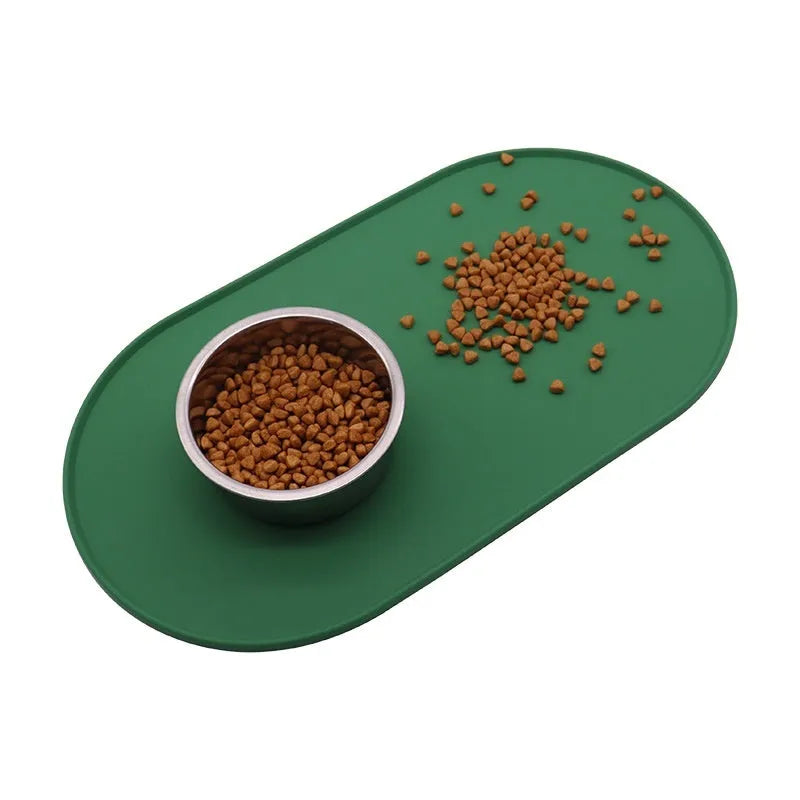 Green silicone cat feeding mat with raised edge under a ceramic food and water bowl on a wooden floor.