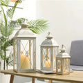Black and white wrought iron floor-standing storm lantern with tempered glass panels in three sizes.