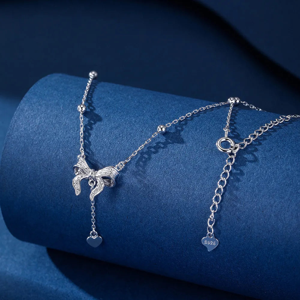 Silver necklace with heart-shaped pendant featuring bow detail on O-ring chain