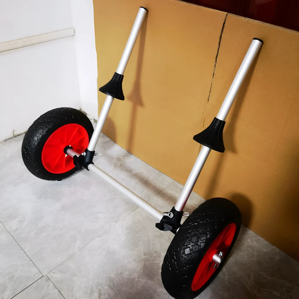 Foldable aluminium kayak trolley with large black pneumatic tyres on a beach, shown carrying a yellow kayak.