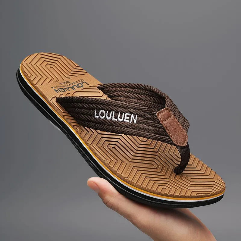 Men's black flip flops with a textured non-slip sole on a sandy beach background.