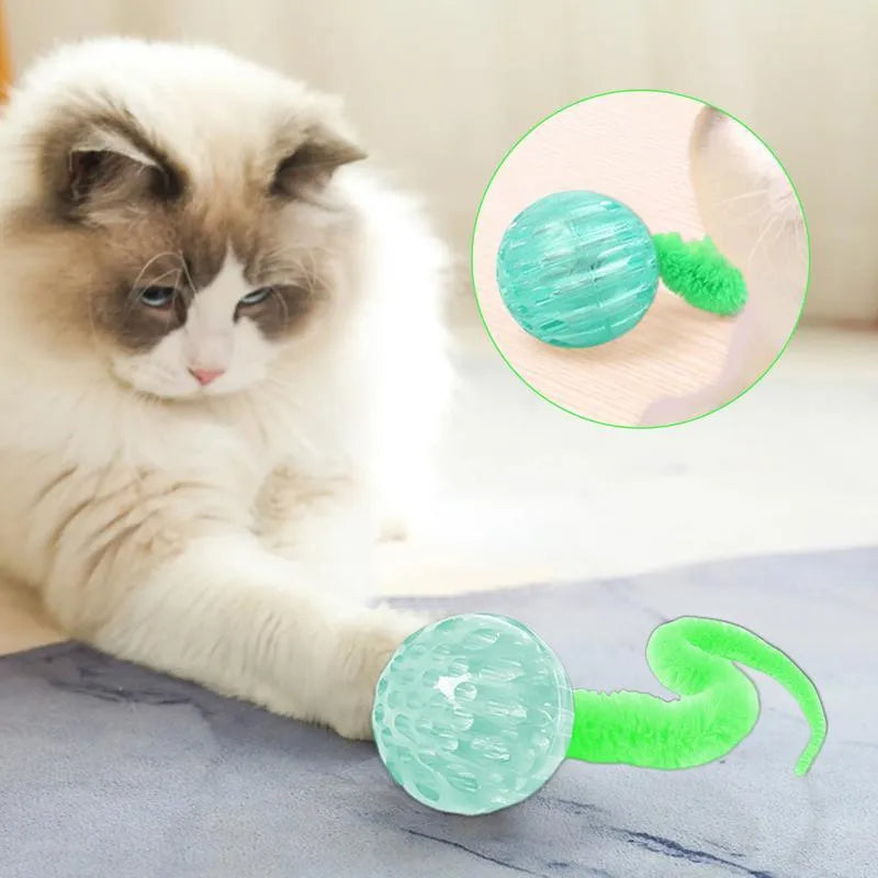 Green bouncy worm-shaped cat toy with a long plush tail on a wooden floor.