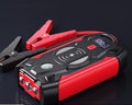 Red 12V car battery jump starter power pack with battery clips on a black background.