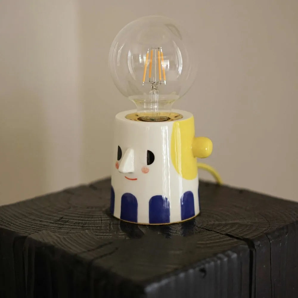 Handmade ceramic bedside lamp with a white ball headlight on a wooden table.