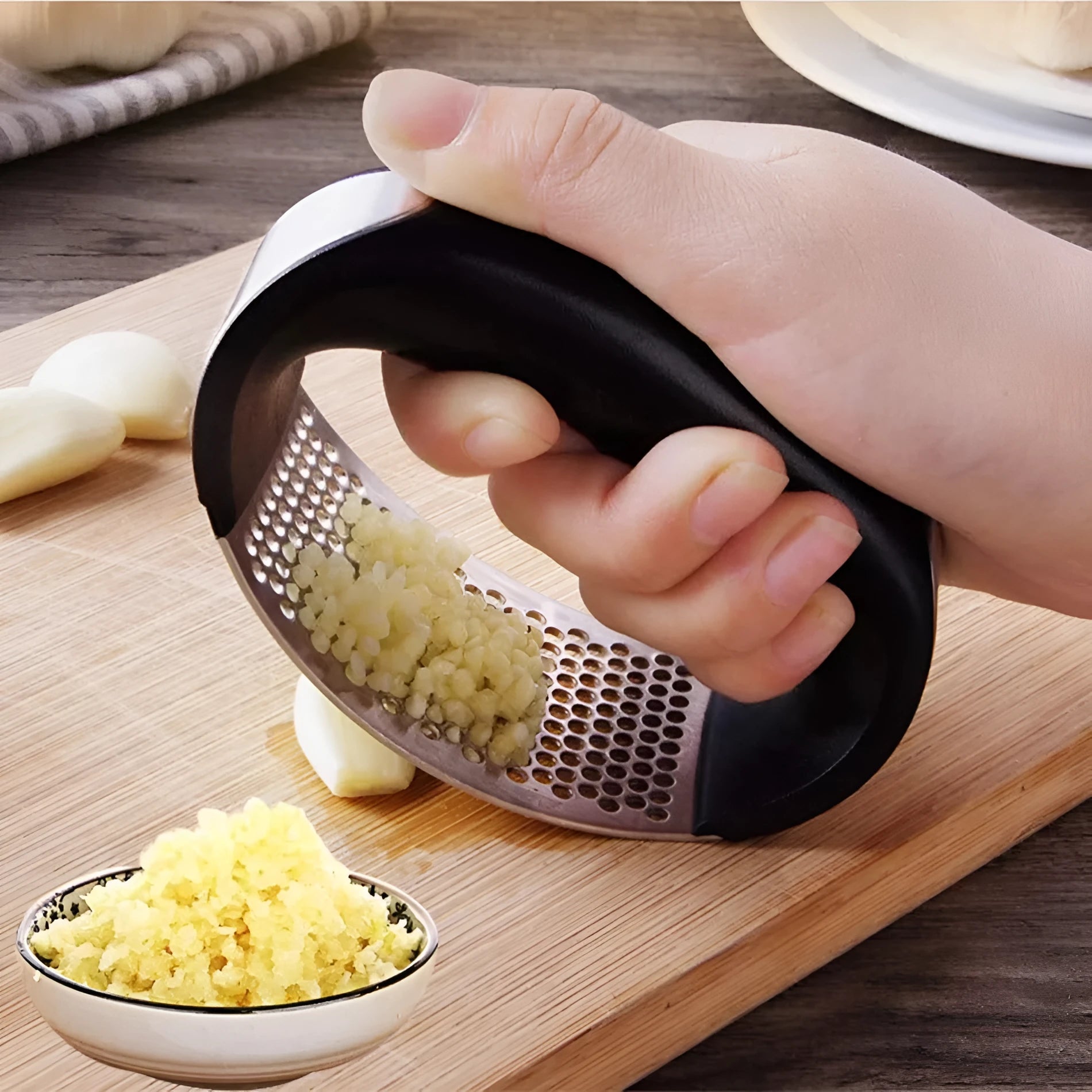 Stainless steel manual garlic press with coloured non-slip handle on a kitchen counter.