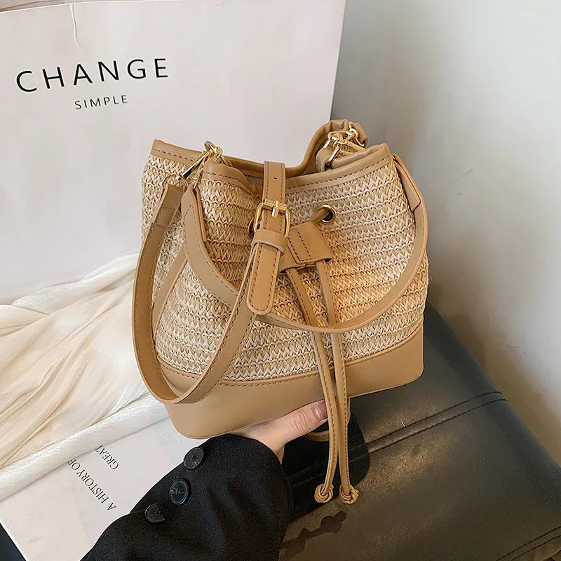 Brown woven straw women's crossbody bucket bag with adjustable strap on a table.
