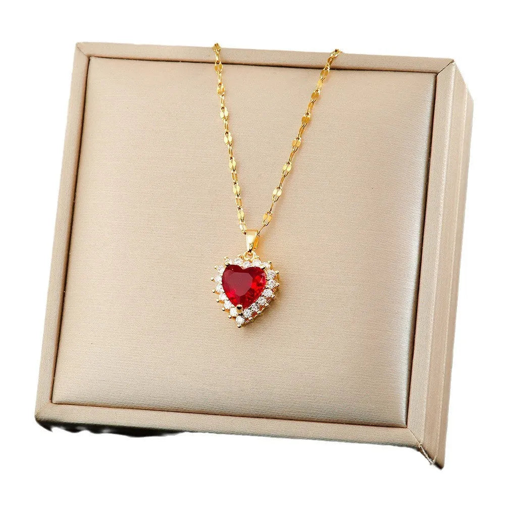 Gold red titanium steel necklace with heart and flower gemstone pendant, matching stud earrings, and ring on a jewellery stand.