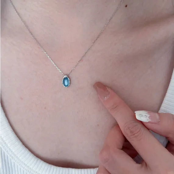 Close-up of a women's navy blue water drop pendant necklace with a platinum-colour electroplated finish on an adjustable cross chain.