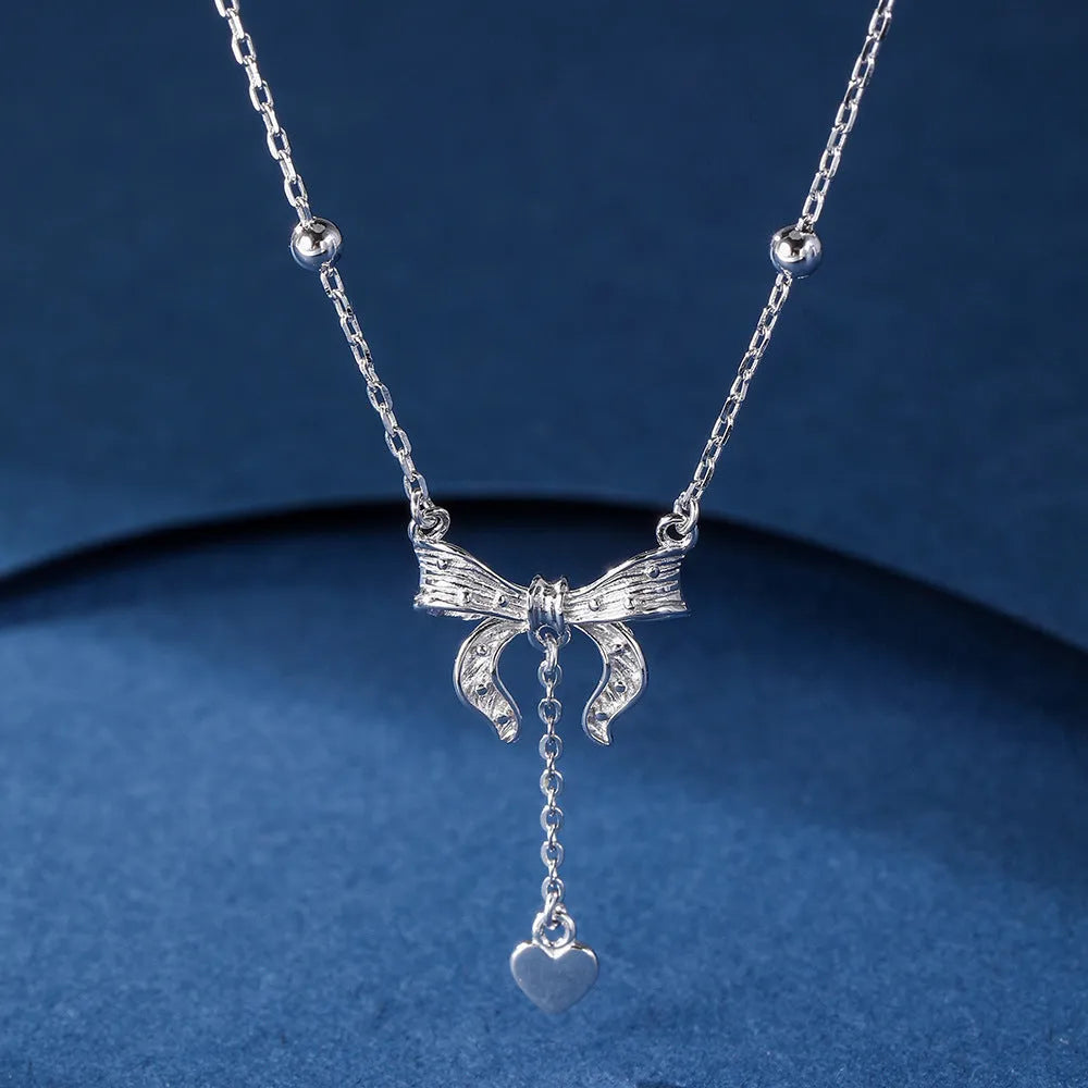 Silver necklace with heart-shaped pendant featuring bow detail on O-ring chain