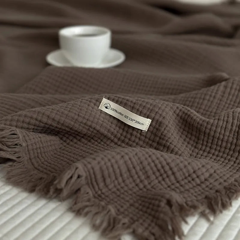 Four-layer gauze cotton blanket with tassel trim in avocado green, laid flat.