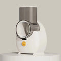 White electric vegetable slicer with suction base, feeding port, pressing rod, and multiple blades on a kitchen counter.