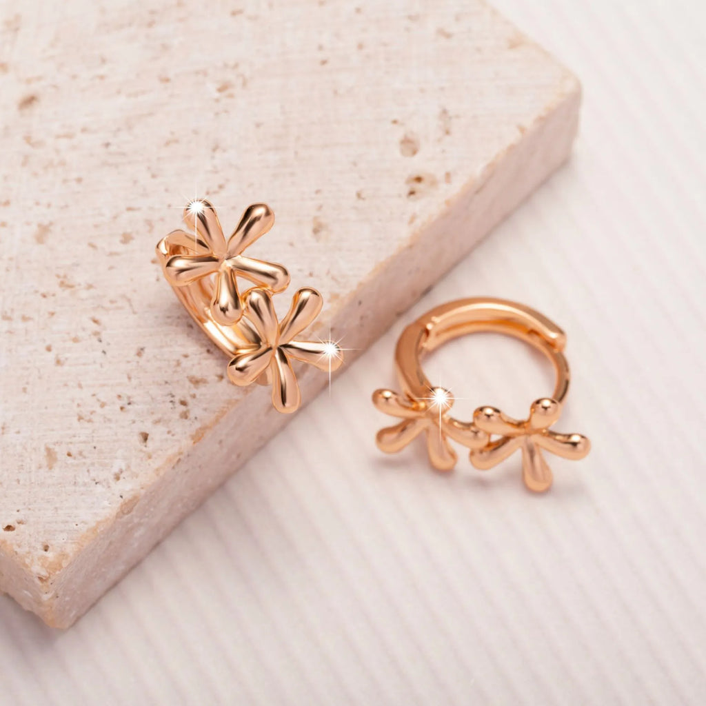 Close-up of rose gold drop earrings with 3D floral and waterdrop design on a white background.