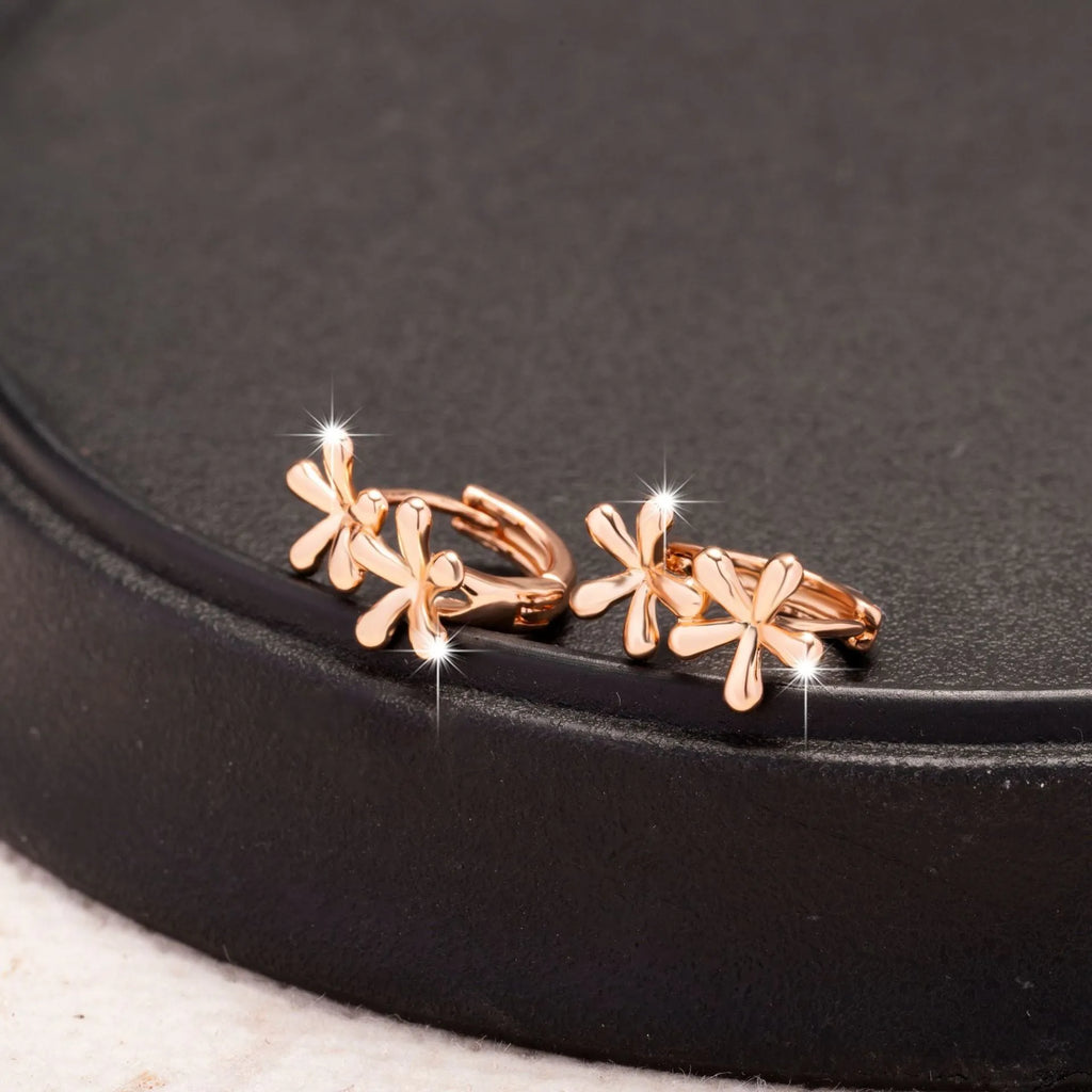 Close-up of rose gold drop earrings with 3D floral and waterdrop design on a white background.