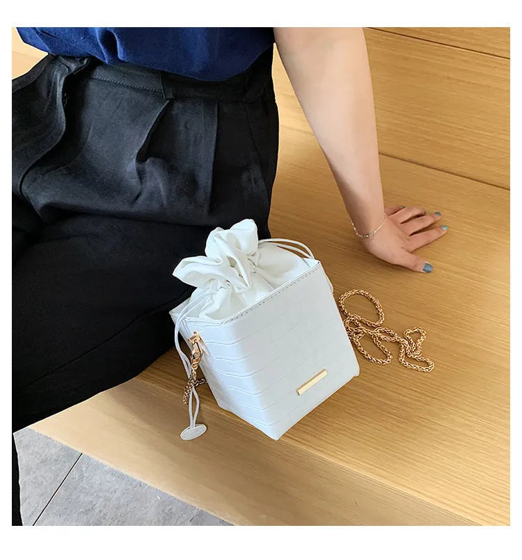 Small black bucket-shaped women's messenger bag with a detachable metal chain strap on a table.