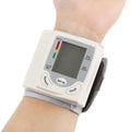 Grey portable wrist blood pressure monitor with digital display on a wrist.