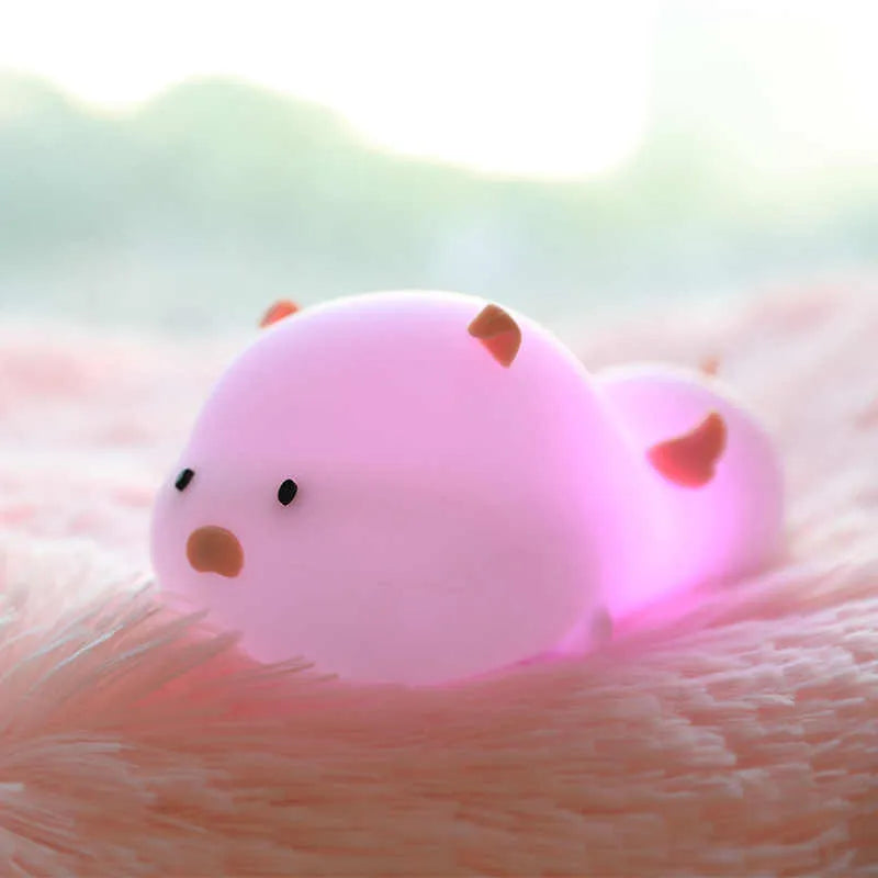 Blue rechargeable pig-shaped silicone night light with soft glow on a bedside table.