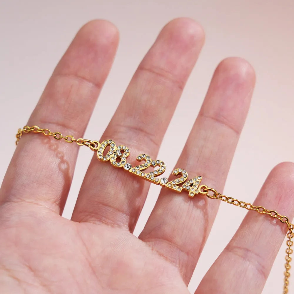 Stainless steel digital bracelet watch with diamond-set numbers on the face, shown in gold tone.