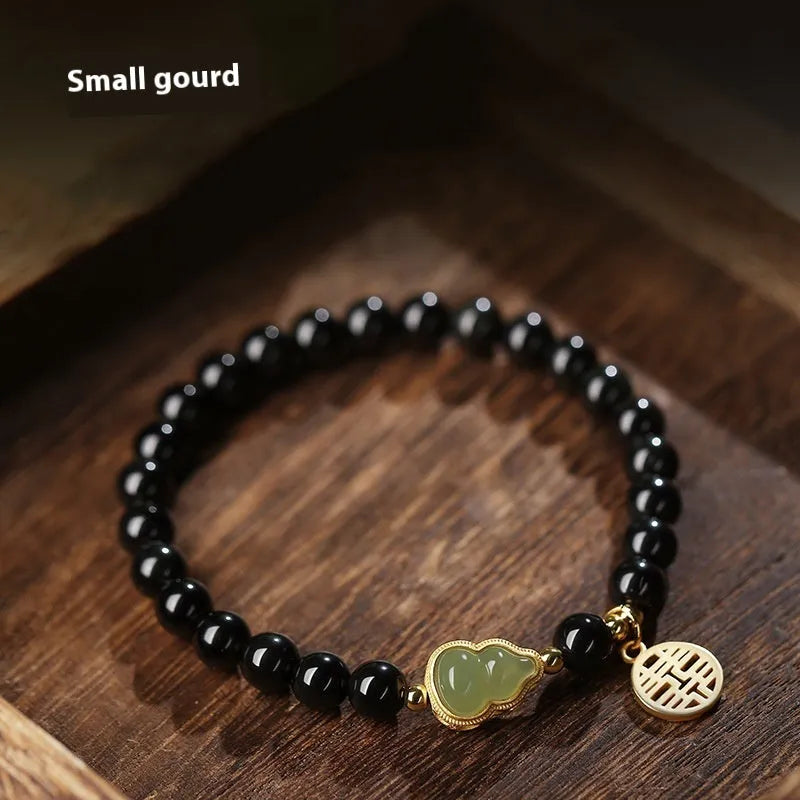 Black obsidian bead bracelet with a carved Hetian jade gourd charm in geometric pattern.