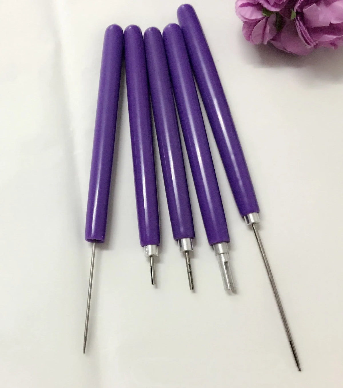 Five purple quilling pens with slotted tips and a stylus laid out on a surface