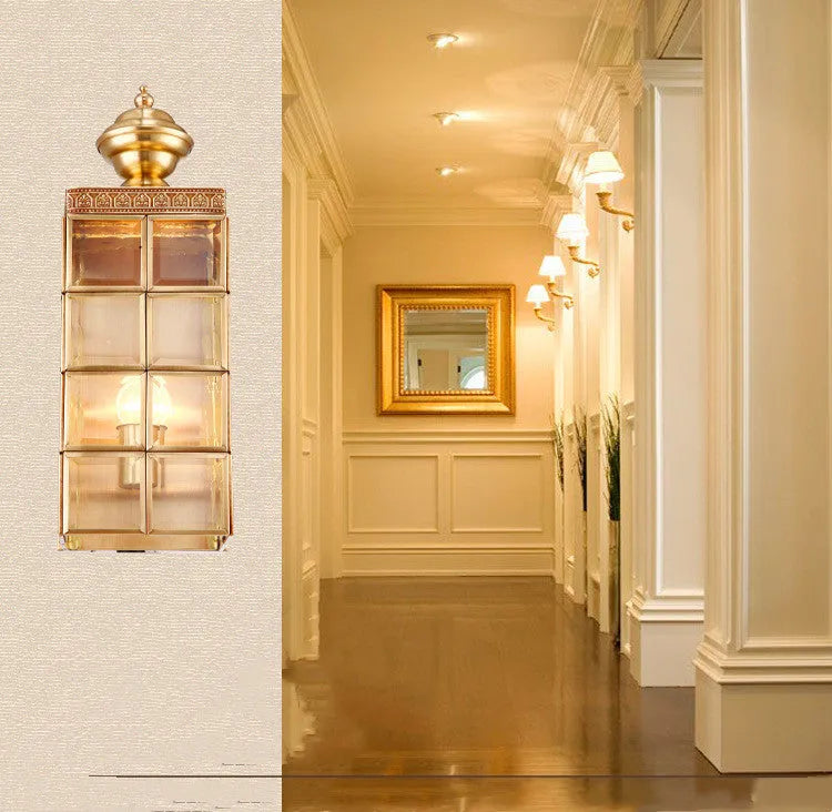 Full copper wall lamp with glass shade and gold finish on a brick balcony wall