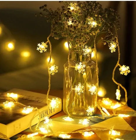Battery powered LED snowflake string lights in warm white on a garden tree branch for Christmas decoration