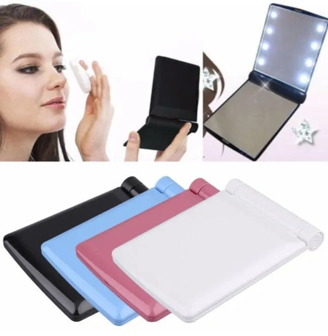 Folding LED pocket cosmetic mirror in black, blue, pink, or white with protective lid and compact plastic casing for handbag or travel use.