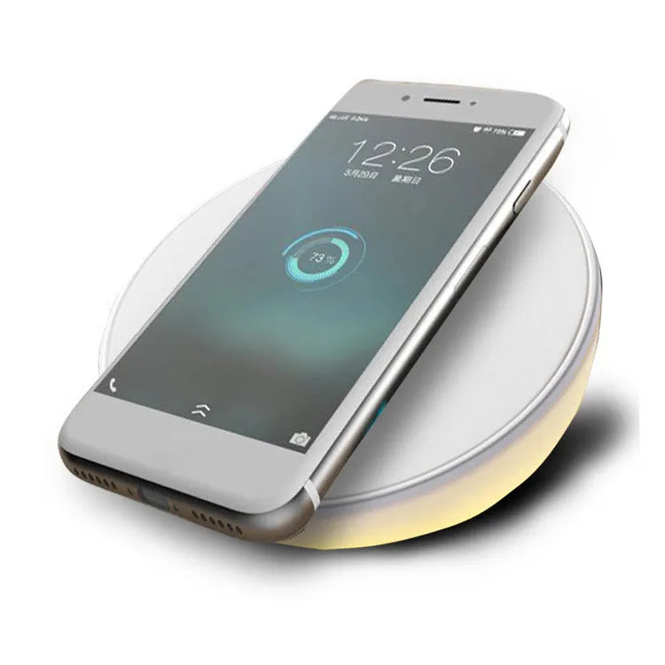 White wireless charging pad with digital clock display and night light, shown on a wooden surface.
