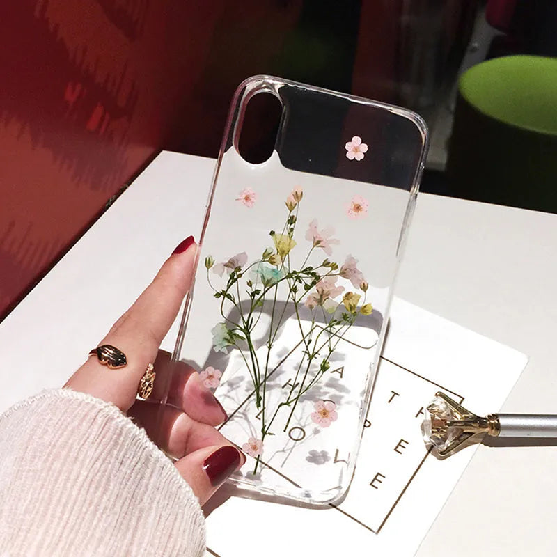 Handmade clear iPhone case with dried pink flowers preserved in epoxy resin visible through TPU back