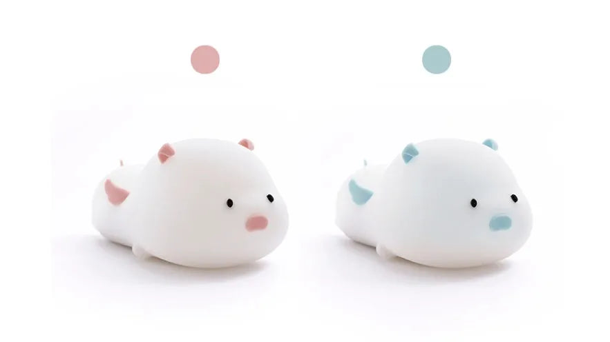 Blue rechargeable pig-shaped silicone night light with soft glow on a bedside table.