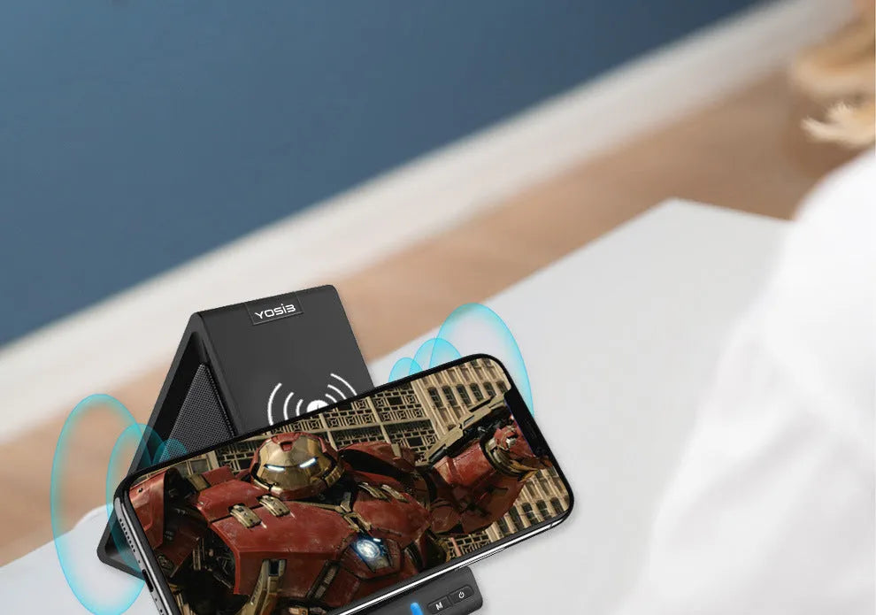 Black multifunctional Bluetooth speaker with integrated mobile phone stand and wireless charging pad on a desk