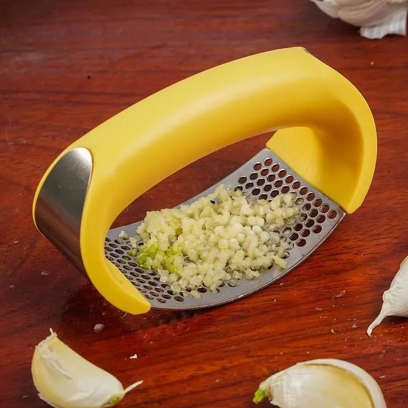 Stainless steel manual garlic press with coloured non-slip handle on a kitchen counter.