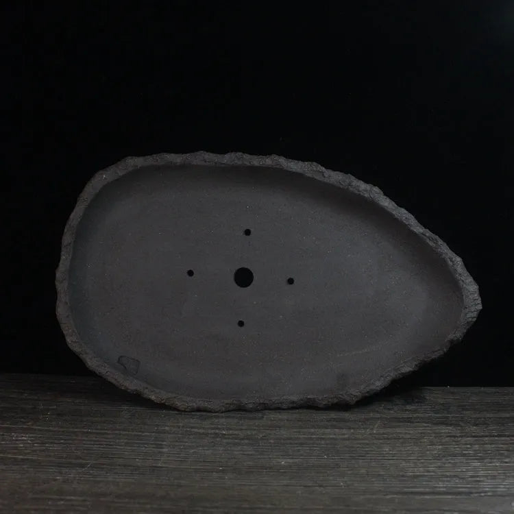 Handmade purple clay flower pot with drainage hole on a wooden floor