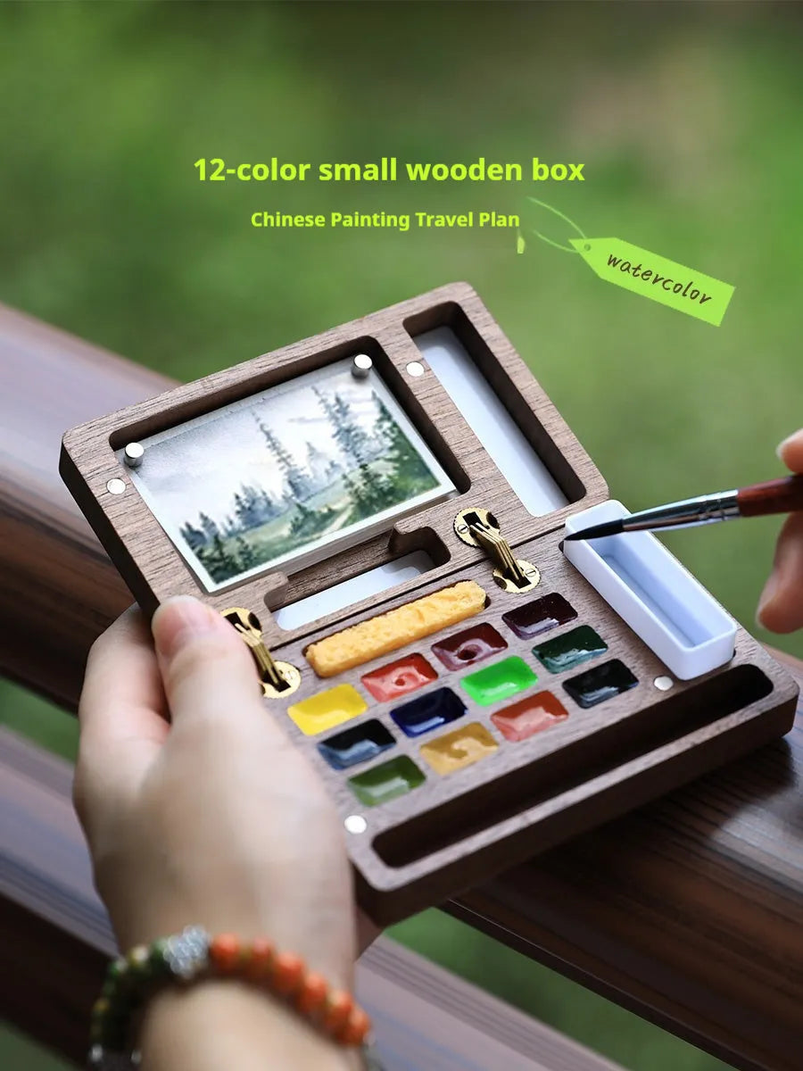 Mini walnut wood watercolour paint box open to show a set of professional paint pigments.