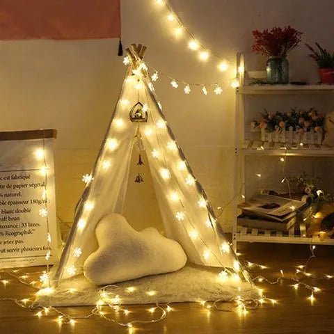 Battery powered LED snowflake string lights in warm white on a garden tree branch for Christmas decoration