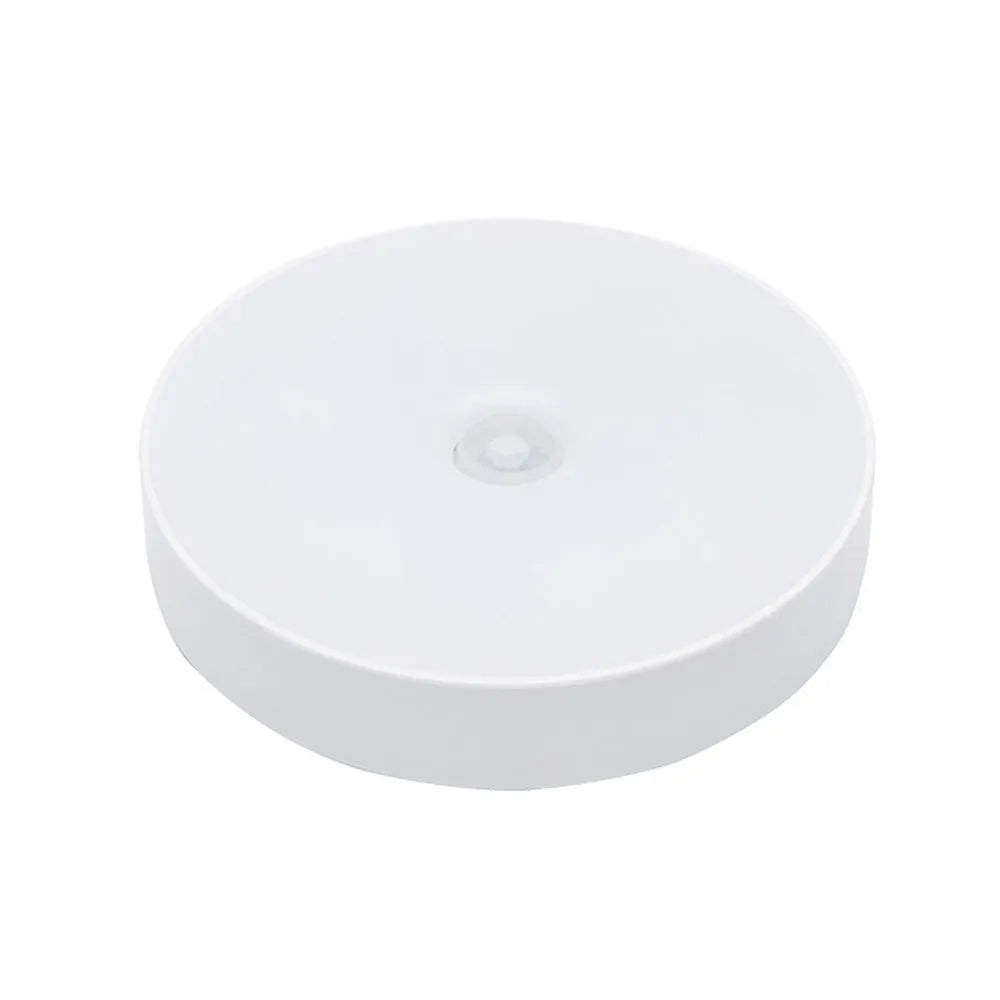 Small round beige and white LED motion sensor night light with USB charging cable and adhesive tape.