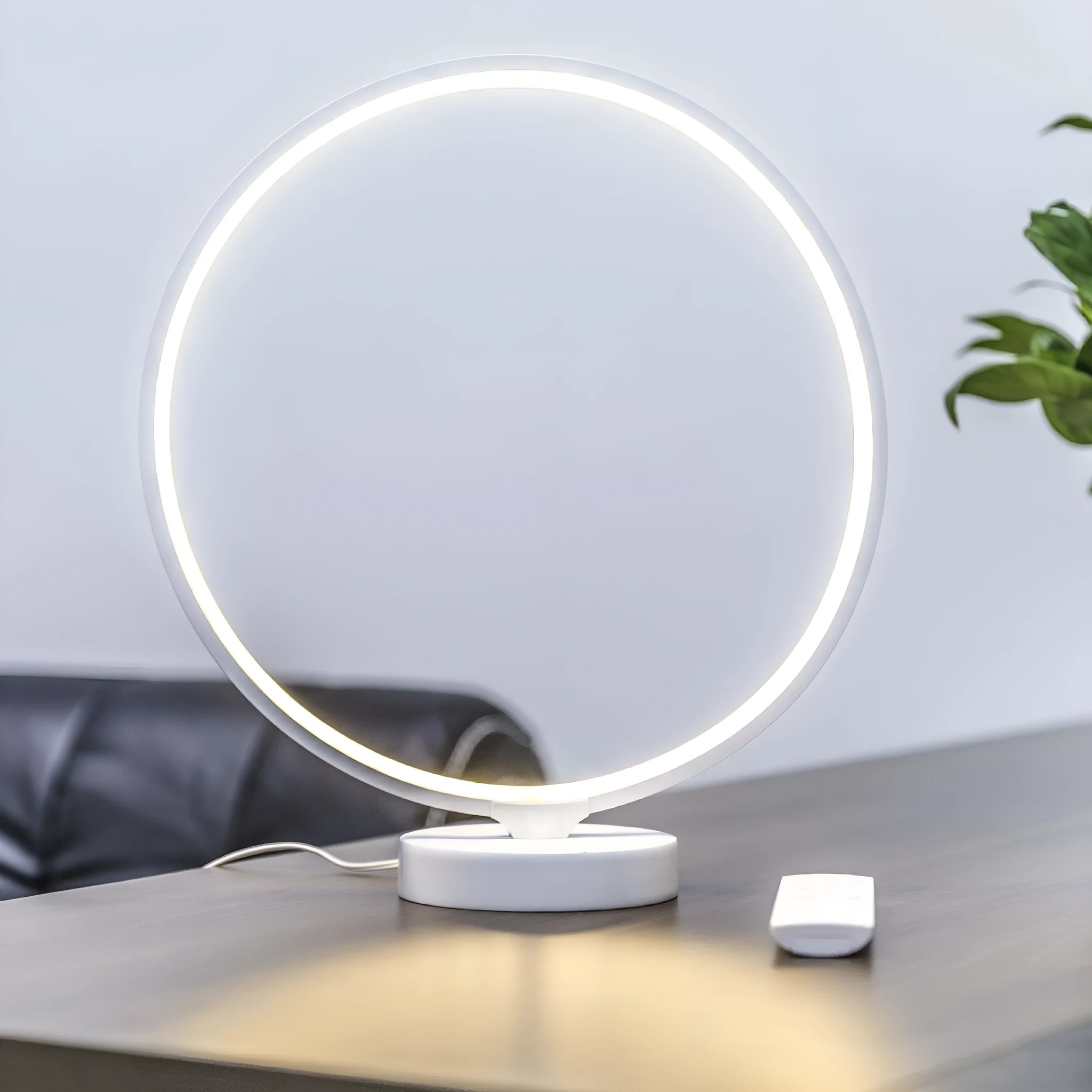 White Full Moon table lamp with remote control on a wooden surface, showing its round silicone diffuser and aluminium base.