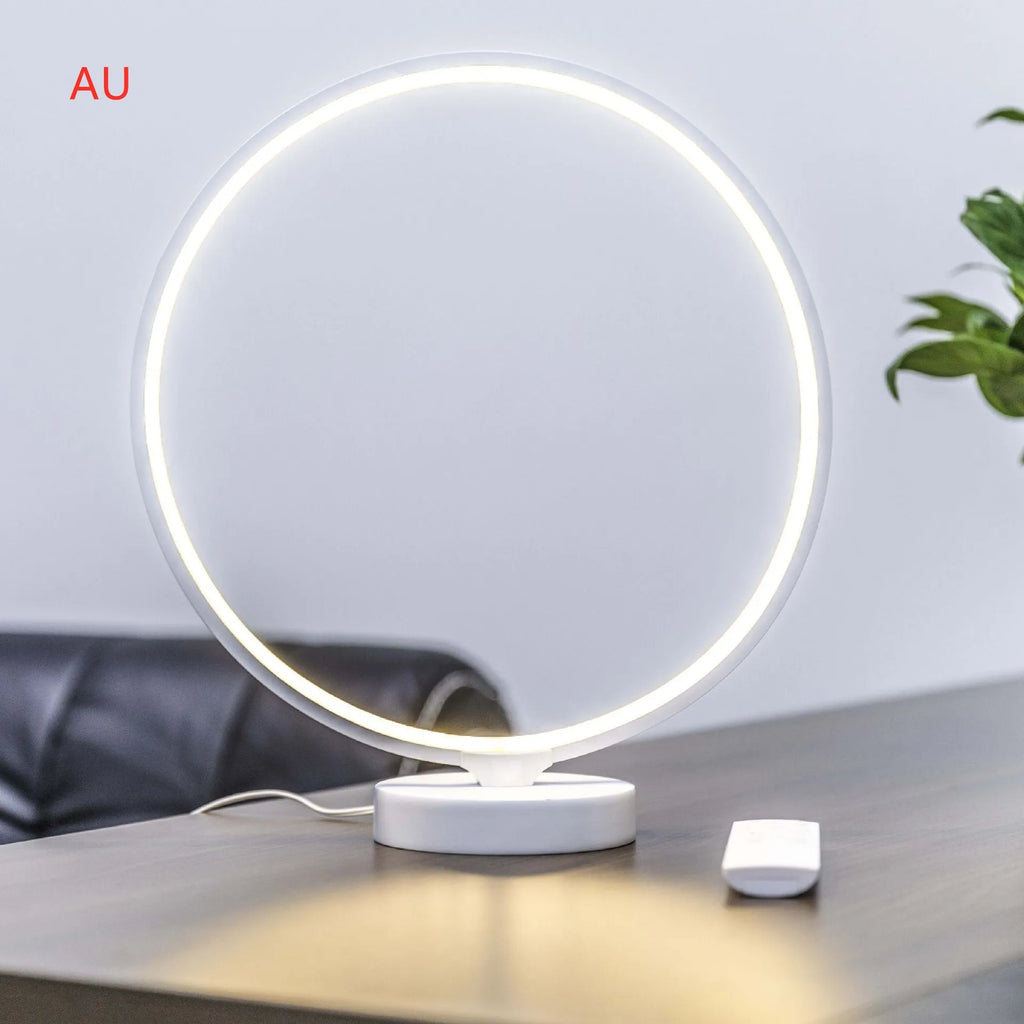White Full Moon table lamp with remote control on a wooden surface, showing its round silicone diffuser and aluminium base.