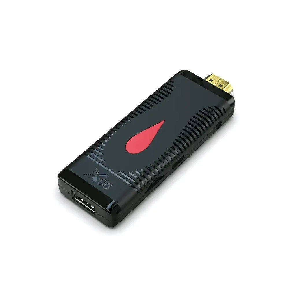 Compact black smart TV set-top box dongle with remote control, HDMI cable, and power adapter on a wooden table.