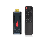 Compact black smart TV set-top box dongle with remote control, HDMI cable, and power adapter on a wooden table.