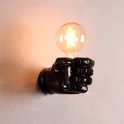 Close-up of a matte black resin fist wall lamp mounted on a grey wall, casting light downwards.